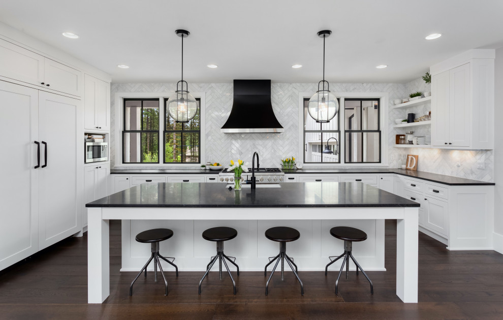 Design ideas for a transitional u-shaped kitchen in Dallas with an undermount sink, shaker cabinets, white cabinets, grey splashback, stainless steel appliances, dark hardwood floors, with island, brown floor and black benchtop.