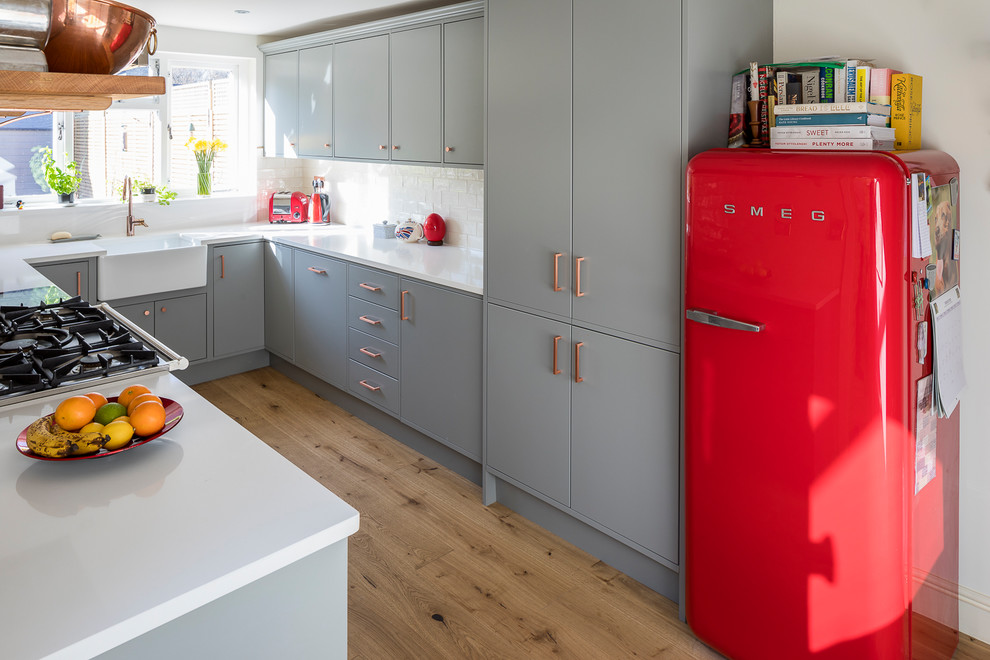 Design ideas for a mid-sized transitional u-shaped separate kitchen in London with flat-panel cabinets, grey cabinets, solid surface benchtops, white splashback, porcelain splashback and no island.
