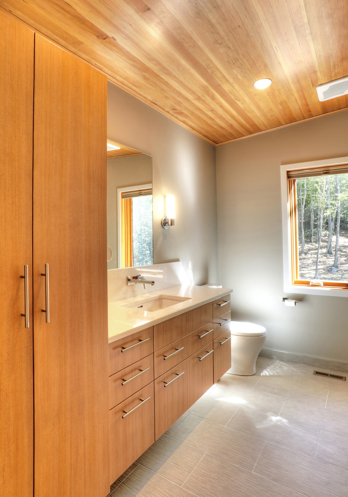 Mid-sized country master bathroom in New York with flat-panel cabinets, medium wood cabinets, an alcove shower, a one-piece toilet, gray tile, porcelain tile, grey walls, porcelain floors, an undermount sink and engineered quartz benchtops.