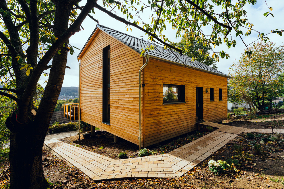 На фото: маленький, двухэтажный, деревянный частный загородный дом в стиле рустика с крышей-бабочкой, черепичной крышей и отделкой планкеном для на участке и в саду