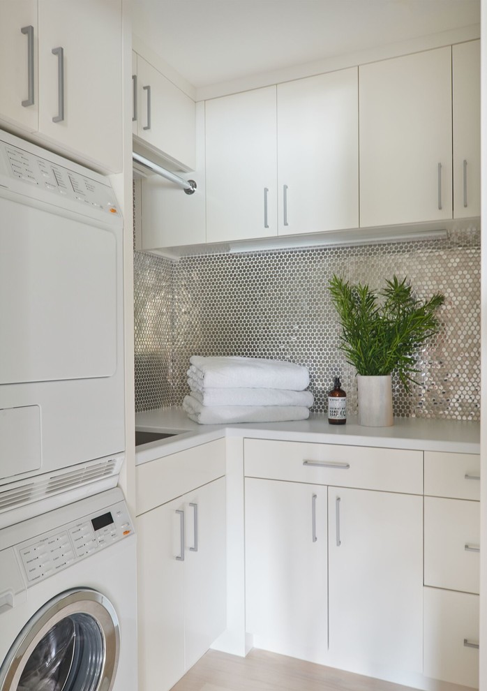Design ideas for a mid-sized contemporary l-shaped dedicated laundry room in New York with an undermount sink, flat-panel cabinets, white cabinets, quartzite benchtops, light hardwood floors, a stacked washer and dryer and white benchtop.