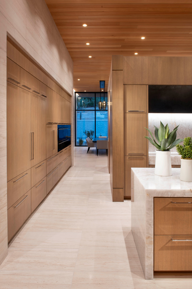 This is an example of an expansive contemporary kitchen in Phoenix with an undermount sink, flat-panel cabinets, light wood cabinets, quartzite benchtops, panelled appliances, limestone floors, multiple islands, white benchtop and wood.
