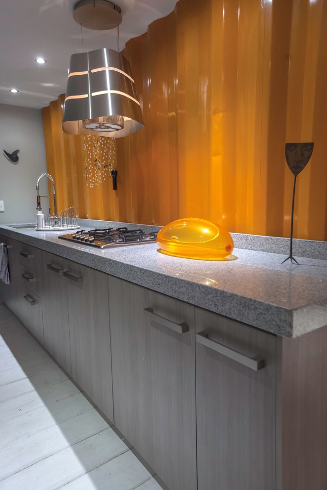 Photo of a small industrial single-wall open plan kitchen in Other with a double-bowl sink, shaker cabinets, grey cabinets, granite benchtops, orange splashback, metal splashback, stainless steel appliances, light hardwood floors and no island.