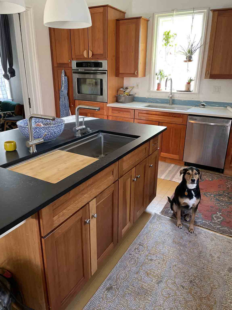 Inredning av ett eklektiskt stort svart svart kök, med en enkel diskho, skåp i shakerstil, bruna skåp, bänkskiva i kvarts, grönt stänkskydd, stänkskydd i keramik, rostfria vitvaror, en köksö, gult golv och målat trägolv