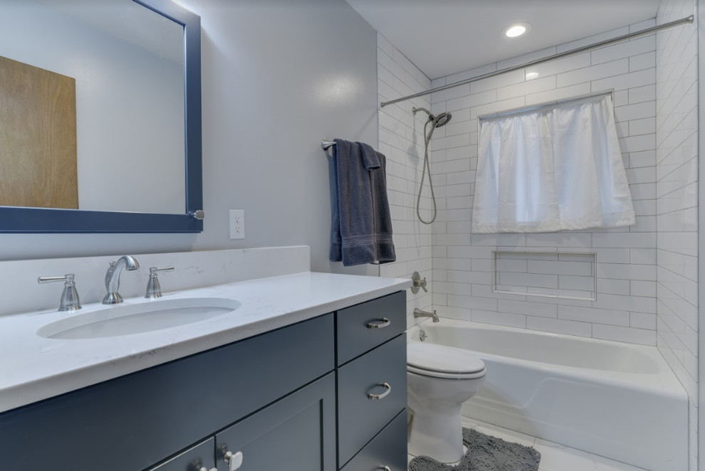 Inspiration for a mid-sized transitional kids bathroom in Portland with shaker cabinets, blue cabinets, an alcove tub, a one-piece toilet, white tile, subway tile, grey walls, porcelain floors, an undermount sink, engineered quartz benchtops, white floor, a shower curtain and white benchtops.