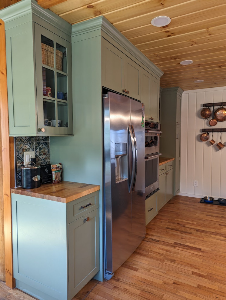 Example of a mid-sized mountain style l-shaped medium tone wood floor, brown floor and wood ceiling eat-in kitchen design with a farmhouse sink, shaker cabinets, green cabinets, granite countertops, multicolored backsplash, ceramic backsplash, stainless steel appliances and black countertops