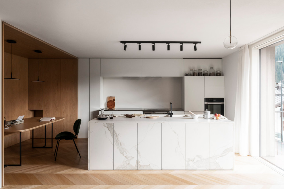 Mid-sized contemporary galley open plan kitchen in Other with an integrated sink, flat-panel cabinets, white cabinets, granite benchtops, white splashback, light hardwood floors, with island, white benchtop and recessed.