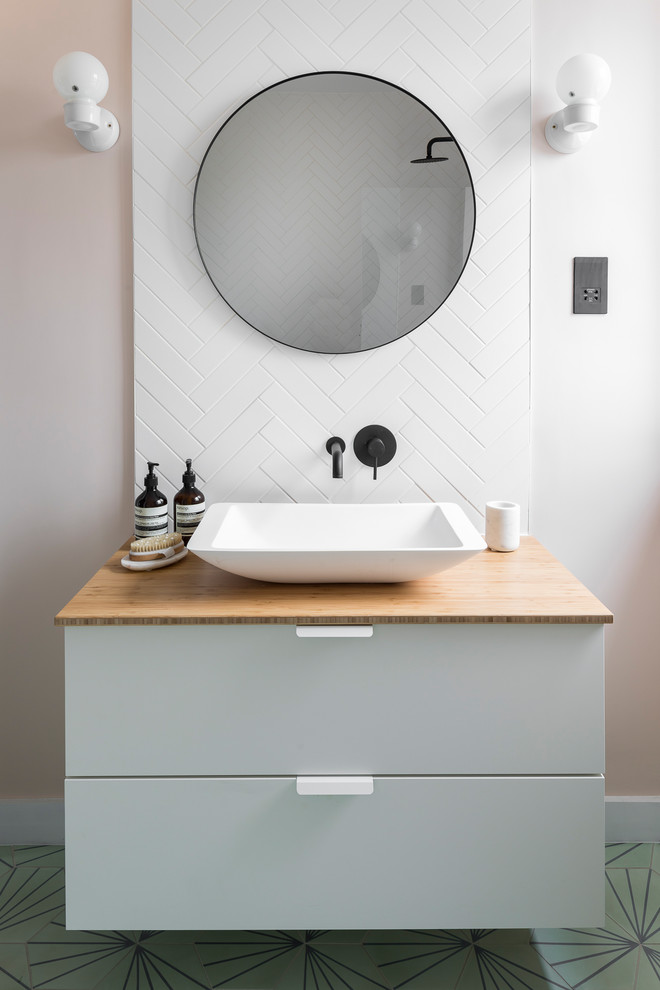 This is an example of a scandinavian bathroom in London with flat-panel cabinets, white cabinets, white tile, white walls, a vessel sink, wood benchtops, green floor and beige benchtops.