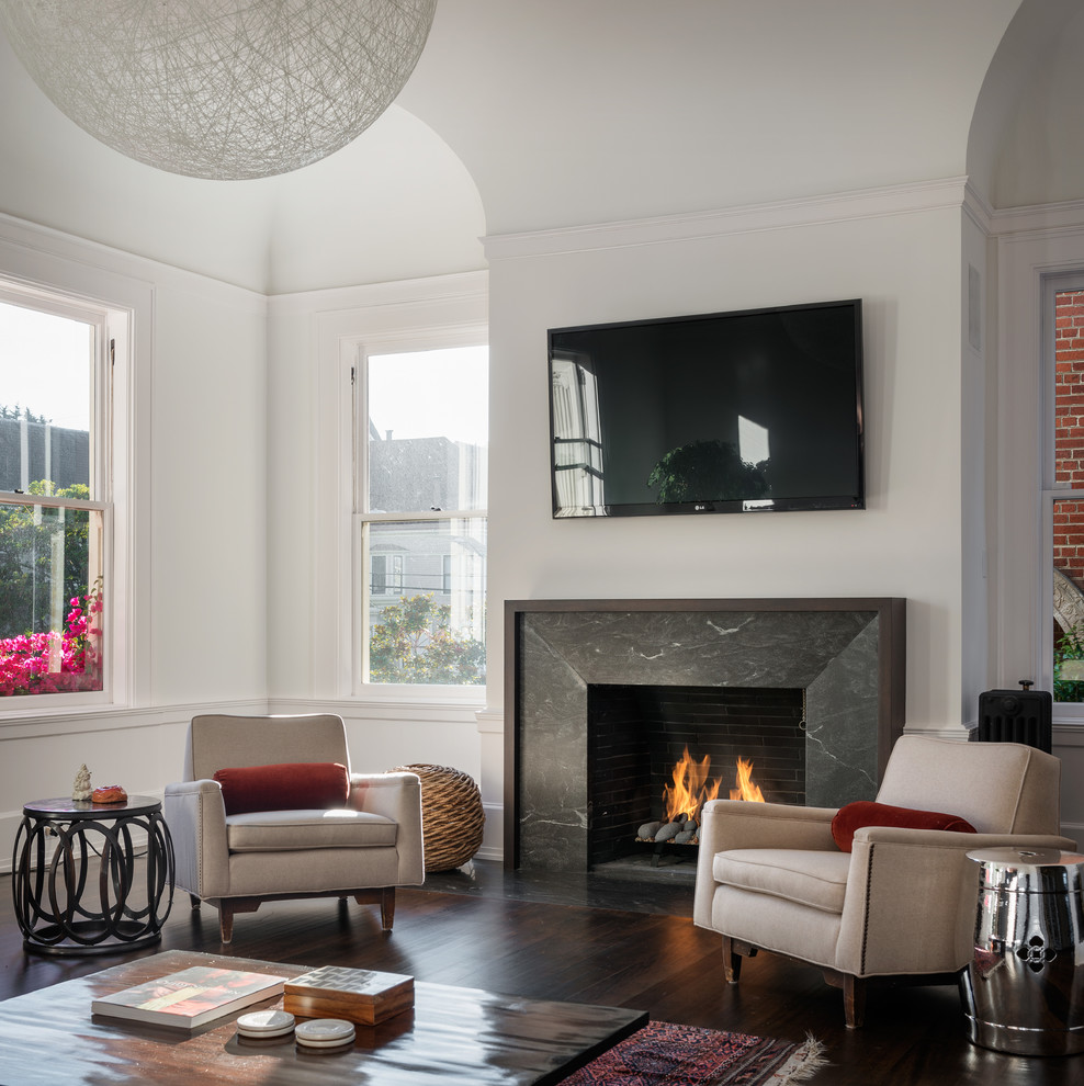 Photo of a transitional living room in San Francisco with white walls, dark hardwood floors, a standard fireplace, a stone fireplace surround and a wall-mounted tv.