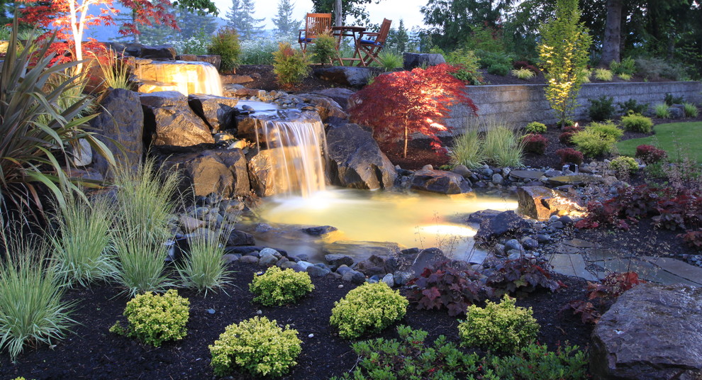 Traditional backyard garden in Seattle with with waterfall and river rock.