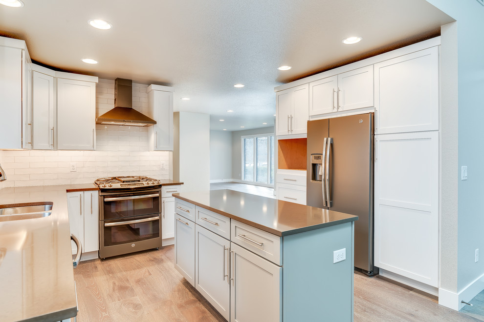 Photo of a small transitional u-shaped open plan kitchen in Boise with a double-bowl sink, shaker cabinets, white cabinets, quartz benchtops, white splashback, subway tile splashback, stainless steel appliances, medium hardwood floors, with island and brown floor.