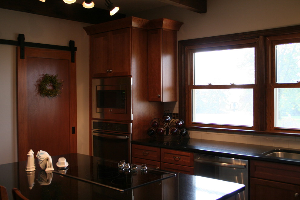 Example of a mid-sized transitional l-shaped medium tone wood floor kitchen design with an undermount sink, medium tone wood cabinets, granite countertops, white backsplash, subway tile backsplash, stainless steel appliances, an island and recessed-panel cabinets