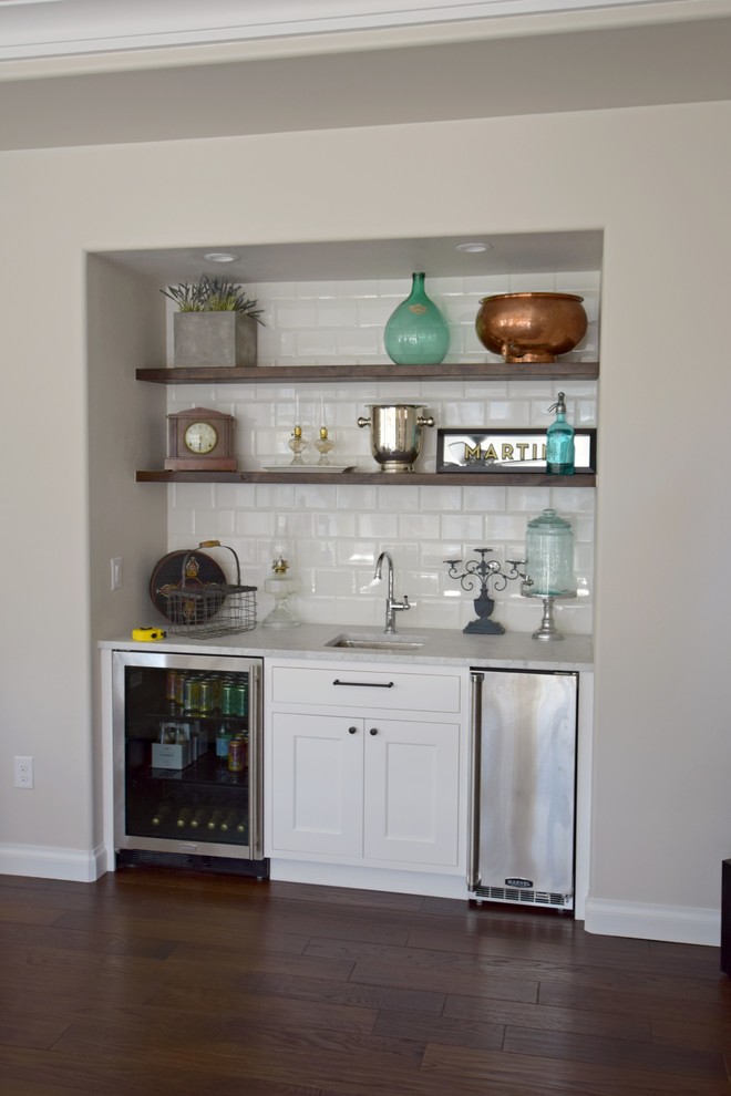 This is an example of a small transitional u-shaped home bar in Denver with an undermount sink, flat-panel cabinets, white cabinets, white splashback, ceramic splashback and medium hardwood floors.