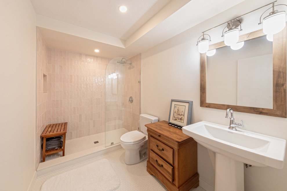 Пример оригинального дизайна: ванная комната среднего размера в стиле неоклассика (современная классика) с фасадами с выступающей филенкой, темными деревянными фасадами, душем в нише, унитазом-моноблоком, розовой плиткой, керамической плиткой, белыми стенами, полом из керамической плитки, душевой кабиной, раковиной с пьедесталом, белым полом, открытым душем, сиденьем для душа, тумбой под одну раковину и напольной тумбой