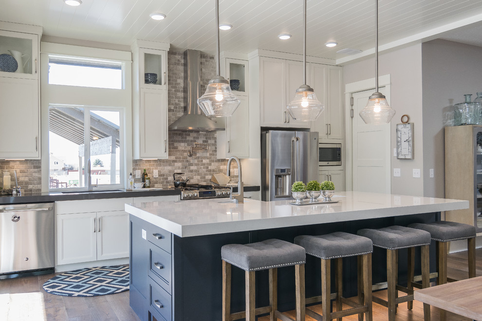 Inspiration for a transitional galley open plan kitchen in Salt Lake City with recessed-panel cabinets, blue cabinets, grey splashback, stainless steel appliances, medium hardwood floors and with island.