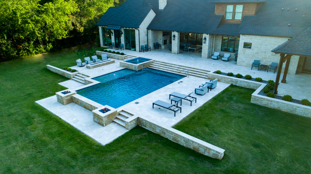 Photo of a large country backyard custom-shaped lap pool in Dallas with a water feature and natural stone pavers.