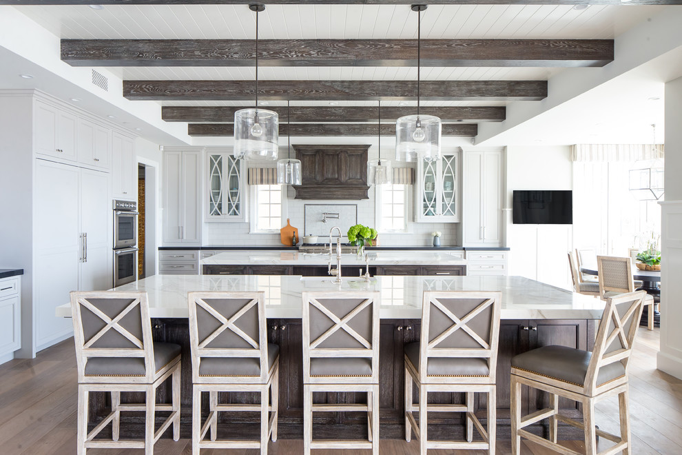 Inspiration for a beach style galley kitchen in Orange County with recessed-panel cabinets, dark wood cabinets, white splashback, subway tile splashback, black appliances, medium hardwood floors, multiple islands and brown floor.