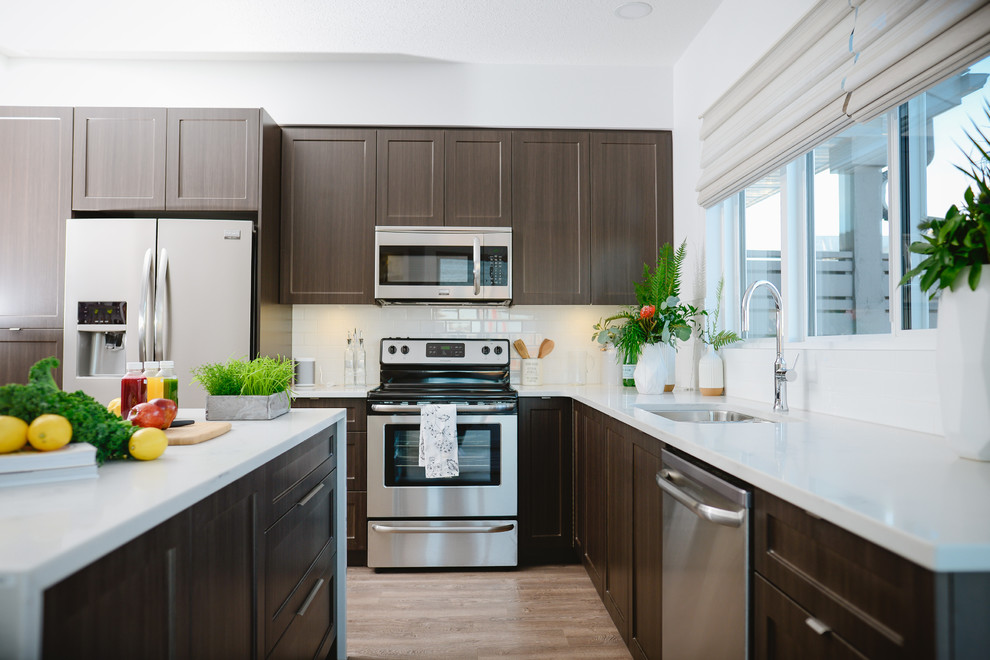 Mid-sized transitional l-shaped medium tone wood floor open concept kitchen photo in Calgary with an undermount sink, recessed-panel cabinets, dark wood cabinets, stainless steel appliances and an island
