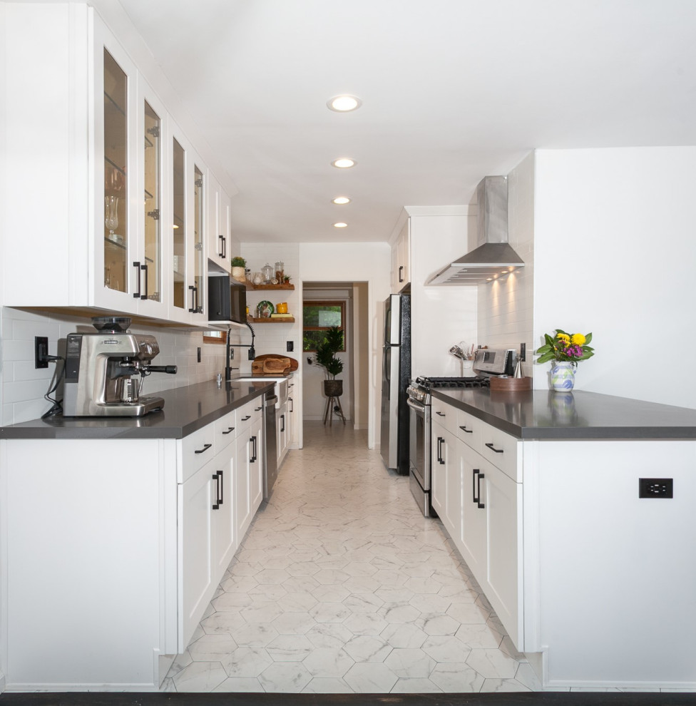 Photo of a mid-sized contemporary galley eat-in kitchen in Los Angeles with a farmhouse sink, glass-front cabinets, white cabinets, quartz benchtops, white splashback, glass tile splashback, black appliances, ceramic floors, a peninsula, white floor and grey benchtop.