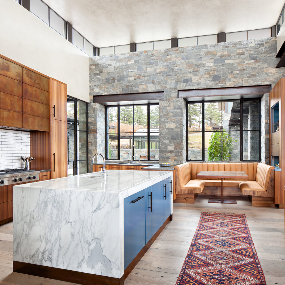 This is an example of a large contemporary u-shaped eat-in kitchen in Denver with a drop-in sink, marble benchtops, white splashback, ceramic splashback, stainless steel appliances, light hardwood floors, with island and beige floor.
