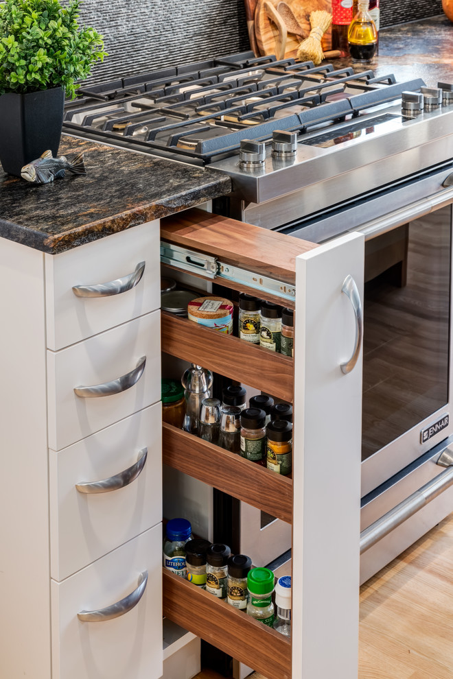 Transitional galley light wood floor home design photo in Calgary with an undermount sink, shaker cabinets, white cabinets, granite countertops, gray backsplash, porcelain backsplash, stainless steel appliances and an island