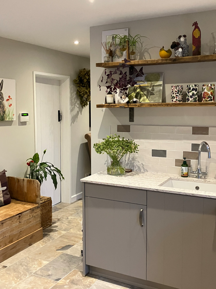 Mid-sized transitional u-shaped utility room in Dorset with a farmhouse sink, flat-panel cabinets, beige cabinets, quartzite benchtops, multi-coloured splashback, ceramic splashback, beige walls, ceramic floors, an integrated washer and dryer, multi-coloured floor and multi-coloured benchtop.