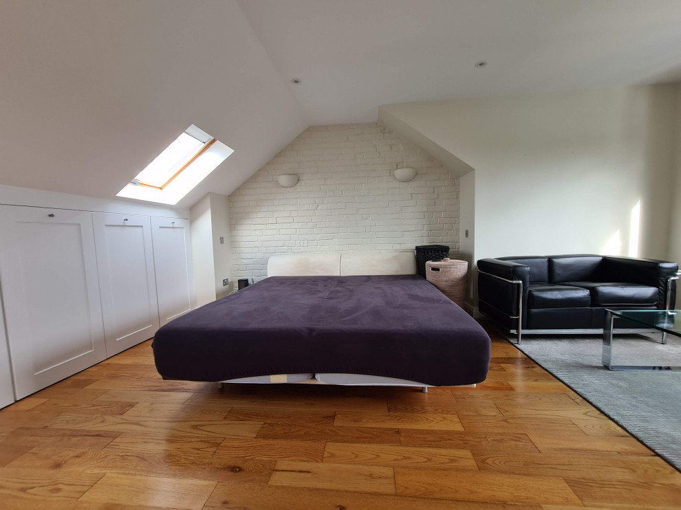 Geräumiges Modernes Schlafzimmer ohne Kamin mit beiger Wandfarbe, dunklem Holzboden, Kaminumrandung aus Backstein, braunem Boden, eingelassener Decke und Ziegelwänden in London