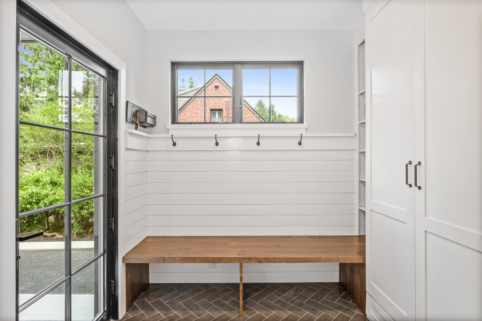 This is an example of a mid-sized country mudroom in Philadelphia with white walls, ceramic floors, a single front door, a black front door, brown floor and planked wall panelling.
