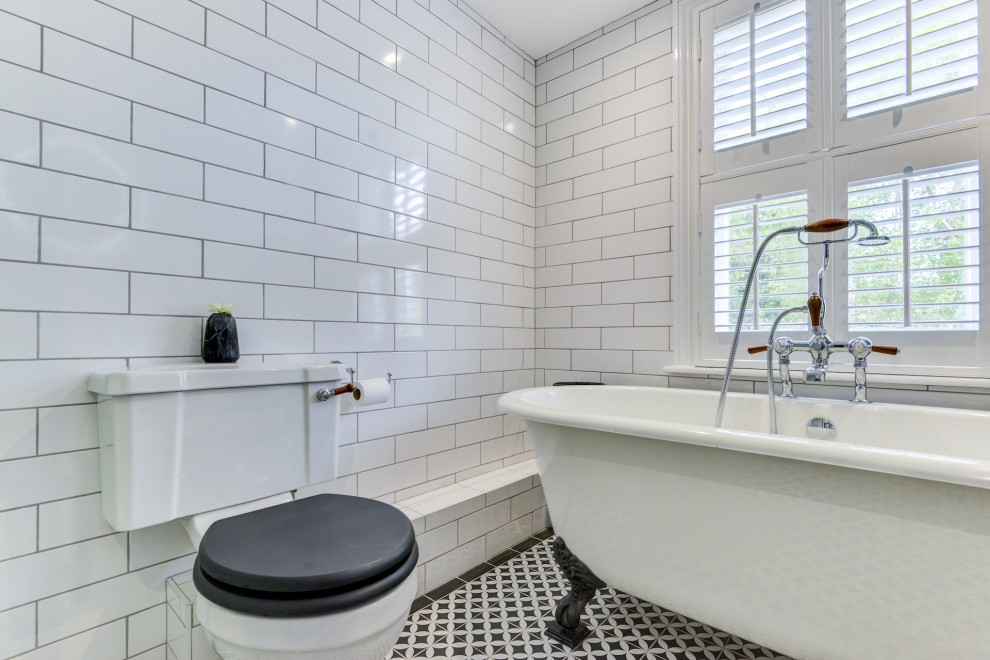 Mid-sized traditional kids bathroom in Sussex with a freestanding tub, a corner shower, a two-piece toilet, white tile, ceramic tile, white walls, ceramic floors, a pedestal sink, tile benchtops, multi-coloured floor, a sliding shower screen, black benchtops and a single vanity.