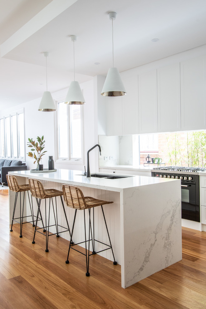 This is an example of a contemporary eat-in kitchen in Sydney with a double-bowl sink, shaker cabinets, white cabinets, quartz benchtops, window splashback, black appliances, light hardwood floors, multiple islands and multi-coloured benchtop.