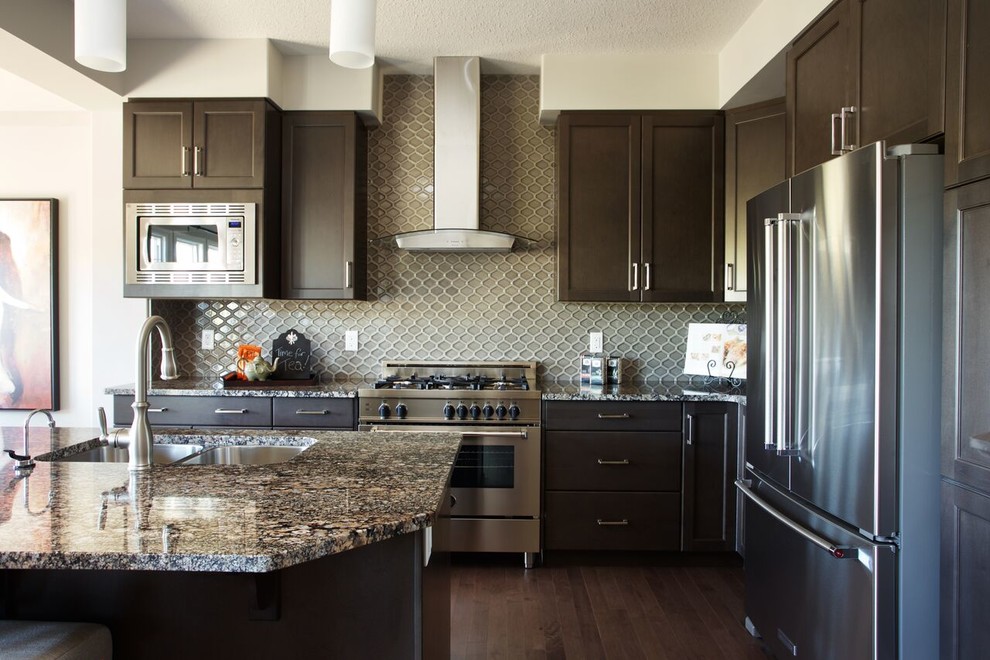 Inspiration for a large transitional l-shaped dark wood floor and brown floor open concept kitchen remodel in Edmonton with a double-bowl sink, raised-panel cabinets, dark wood cabinets, granite countertops, gray backsplash, glass tile backsplash, stainless steel appliances and an island