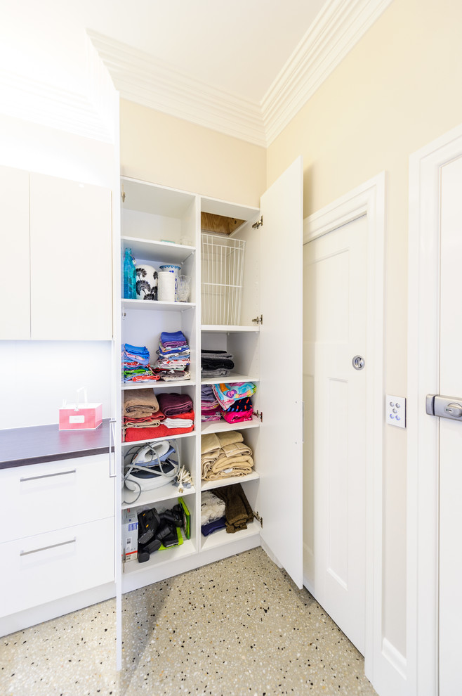 This is an example of a large contemporary l-shaped dedicated laundry room in Melbourne with a drop-in sink, flat-panel cabinets, laminate benchtops, concrete floors, a stacked washer and dryer, white cabinets and white walls.