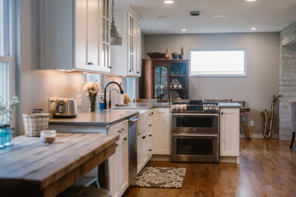 Example of a mid-sized transitional l-shaped medium tone wood floor and brown floor eat-in kitchen design in Columbus with a farmhouse sink, shaker cabinets, white cabinets, solid surface countertops, gray backsplash, matchstick tile backsplash, stainless steel appliances and no island