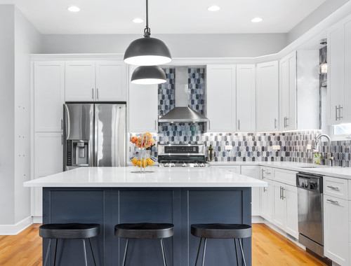 Bright modern Kitchen Cabinet Mississauga with white shaker cabinets, stainless steel appliances, patterned blue tile backsplash, and a navy island topped with a white quartz countertop and pendant lights.