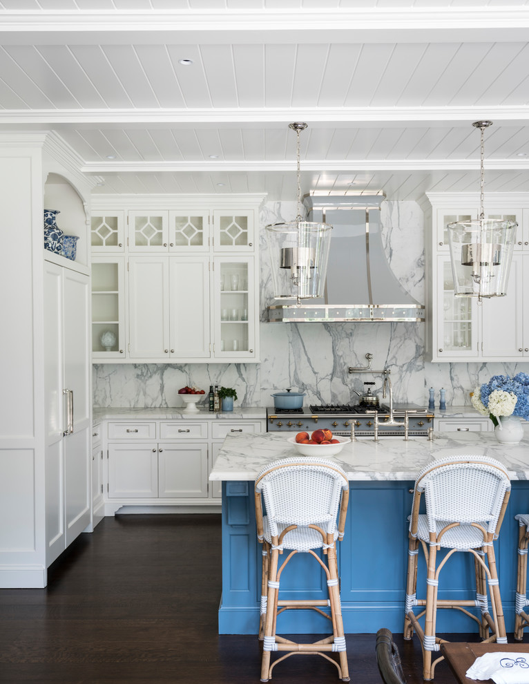 This is an example of an expansive beach style u-shaped eat-in kitchen in New York with a farmhouse sink, glass-front cabinets, white cabinets, marble benchtops, white splashback, marble splashback, panelled appliances, dark hardwood floors, with island and brown floor.