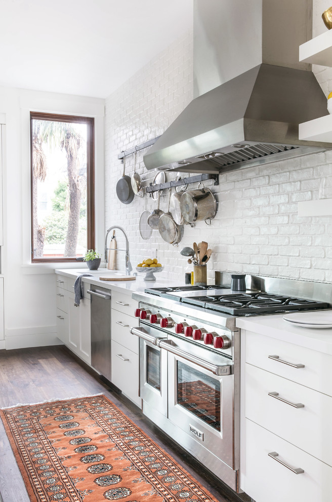 Open concept kitchen - large farmhouse l-shaped dark wood floor open concept kitchen idea in San Francisco with flat-panel cabinets, white cabinets, white backsplash, brick backsplash, stainless steel appliances, a drop-in sink, quartz countertops, an island and white countertops