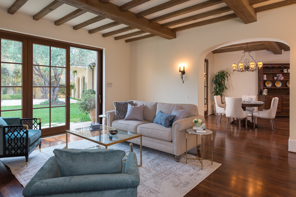 Design ideas for a large mediterranean open concept family room in San Diego with beige walls, medium hardwood floors, a standard fireplace, a plaster fireplace surround and a concealed tv.