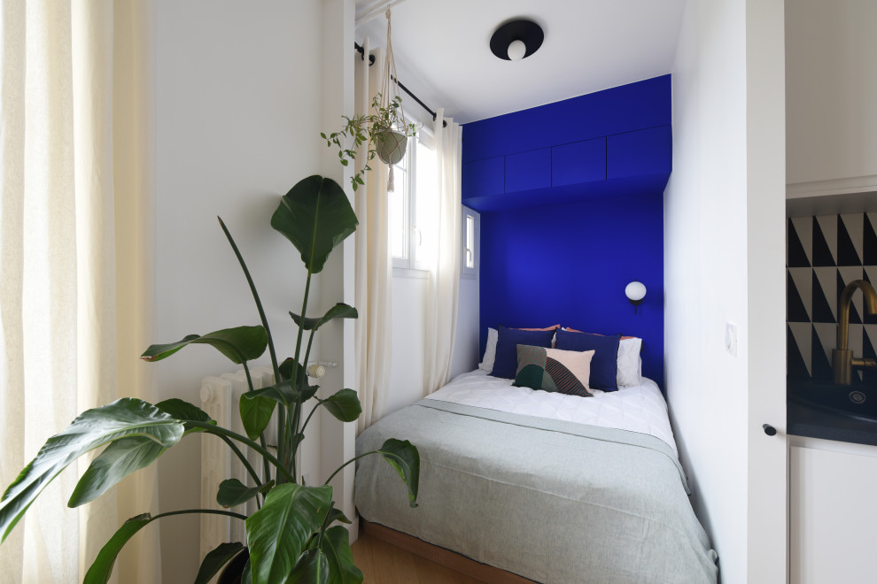 Small contemporary loft-style bedroom in Paris with blue walls and laminate floors.
