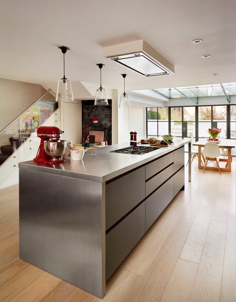 This is an example of a large contemporary open plan kitchen in London with with island, flat-panel cabinets, white cabinets, quartz benchtops, white splashback, glass sheet splashback, stainless steel appliances and an undermount sink.