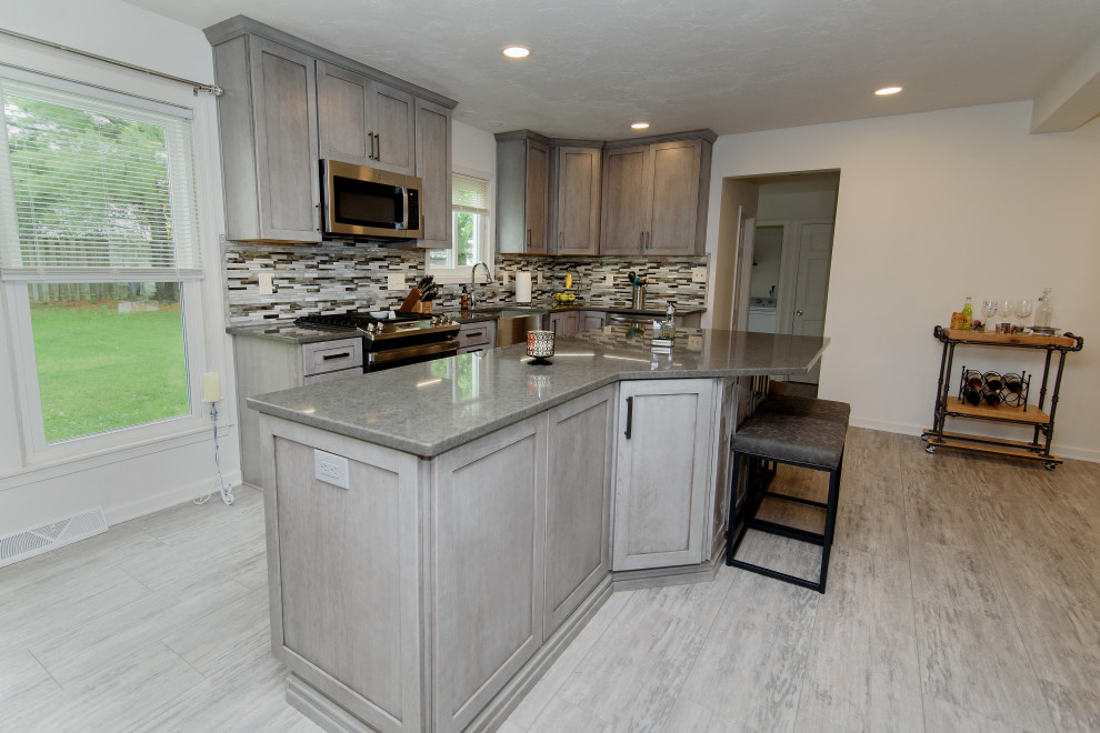 Eat-in kitchen - large transitional u-shaped gray floor eat-in kitchen idea in Baltimore with a farmhouse sink, shaker cabinets, gray cabinets, quartz countertops, multicolored backsplash, glass tile backsplash, stainless steel appliances, an island and gray countertops
