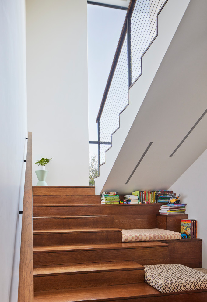 На фото: п-образная деревянная лестница в современном стиле с деревянными ступенями, перилами из тросов и кладовкой или шкафом под ней