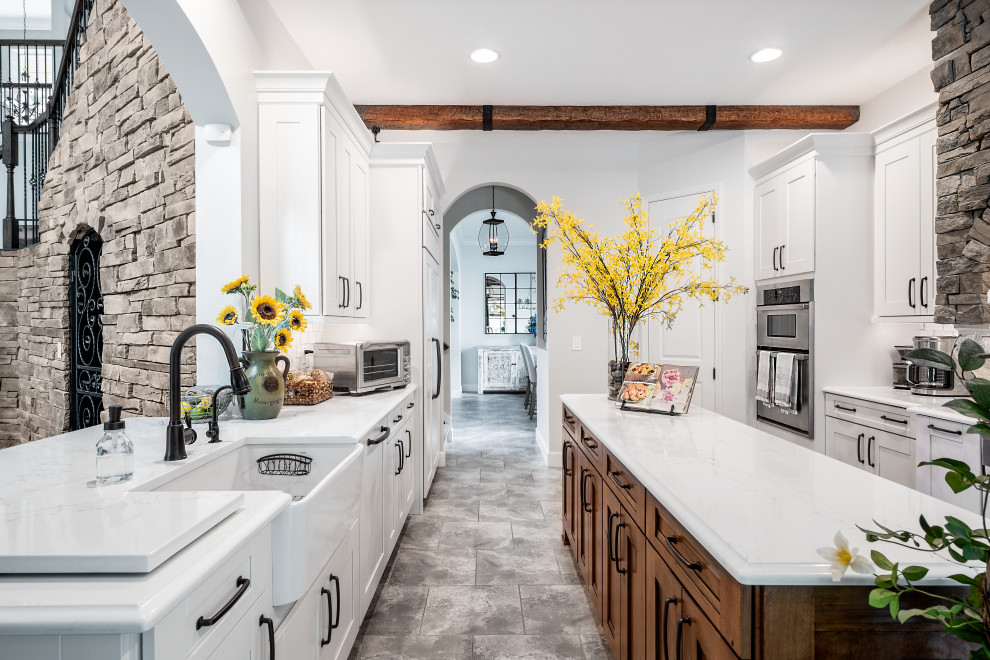 Design ideas for a large transitional galley eat-in kitchen in Tampa with a farmhouse sink, shaker cabinets, white cabinets, quartz benchtops, white splashback, porcelain splashback, stainless steel appliances, porcelain floors, with island, grey floor and white benchtop.