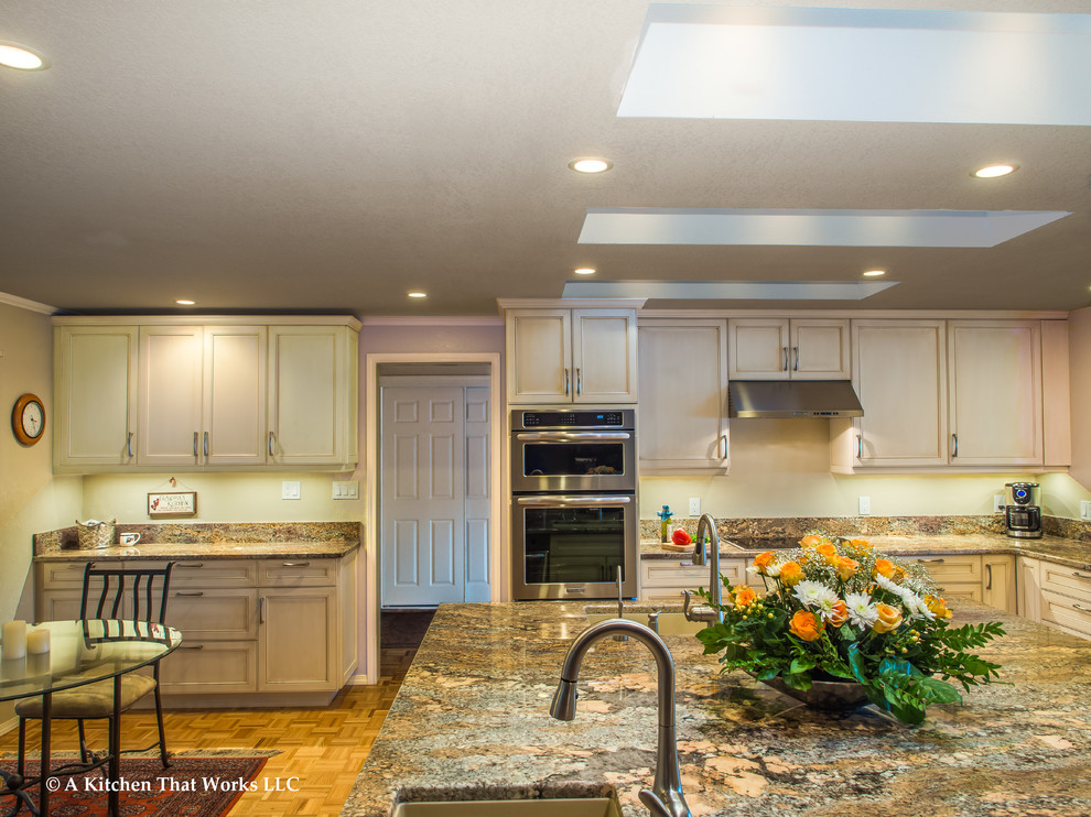 Example of a large transitional u-shaped medium tone wood floor and brown floor eat-in kitchen design in Seattle with an undermount sink, recessed-panel cabinets, white cabinets, granite countertops, stone slab backsplash, stainless steel appliances, an island, brown backsplash and brown countertops