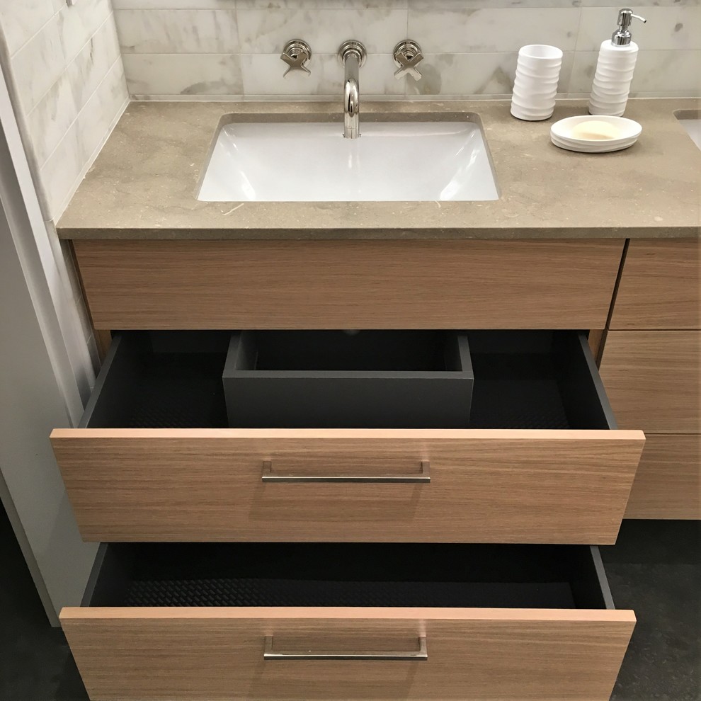 This is an example of a mid-sized contemporary 3/4 bathroom in Other with flat-panel cabinets, light wood cabinets, a curbless shower, a one-piece toilet, white tile, marble, grey walls, concrete floors, an undermount sink, grey floor and a hinged shower door.