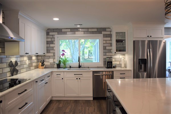 Example of a large transitional l-shaped medium tone wood floor open concept kitchen design in Baltimore with a single-bowl sink, shaker cabinets, white cabinets, quartz countertops, gray backsplash, subway tile backsplash, stainless steel appliances, an island and white countertops