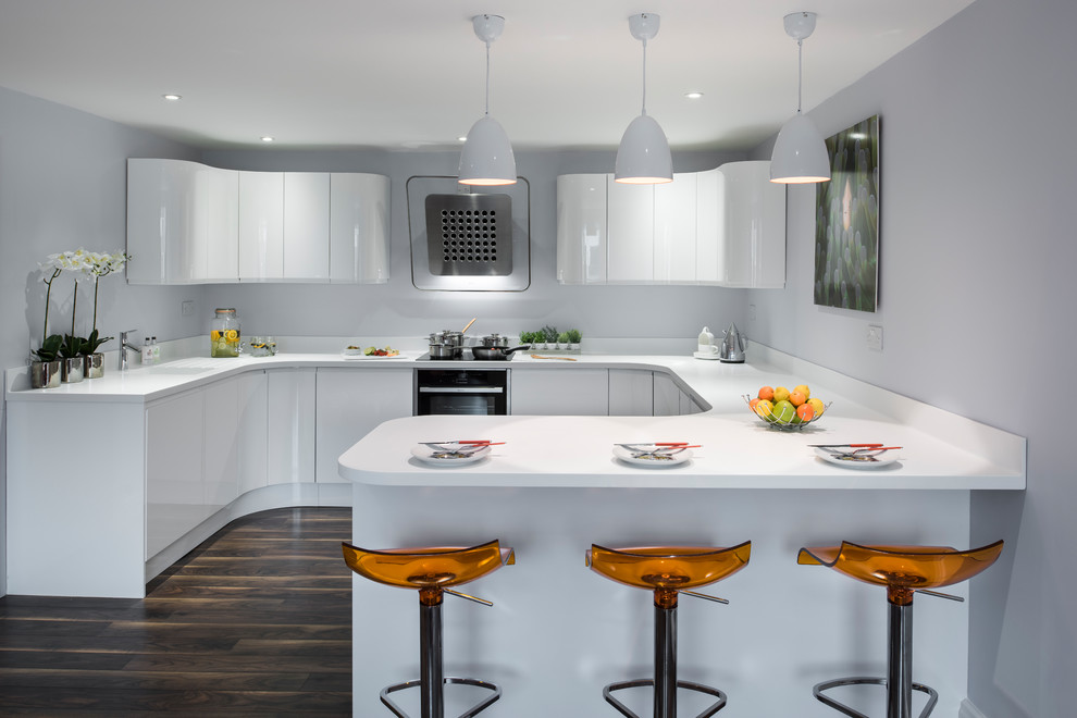 Mid-sized modern u-shaped eat-in kitchen in West Midlands with a drop-in sink, white cabinets, white splashback, stainless steel appliances, dark hardwood floors, a peninsula, brown floor, white benchtop and flat-panel cabinets.