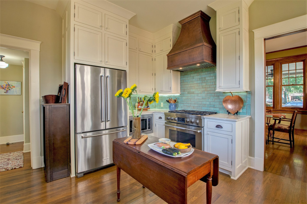 Inspiration for a mid-sized arts and crafts eat-in kitchen in Little Rock with a farmhouse sink, shaker cabinets, white cabinets, marble benchtops, green splashback, terra-cotta splashback, stainless steel appliances, medium hardwood floors, no island, brown floor and beige benchtop.