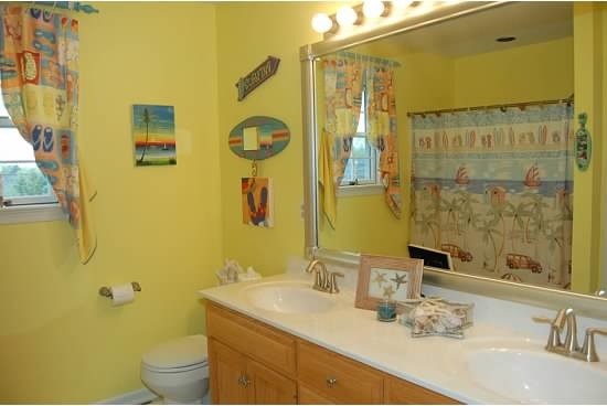 Inspiration for a mid-sized beach style kids bathroom in Philadelphia with raised-panel cabinets, light wood cabinets, an alcove tub, a two-piece toilet, yellow walls, vinyl floors, an integrated sink and solid surface benchtops.