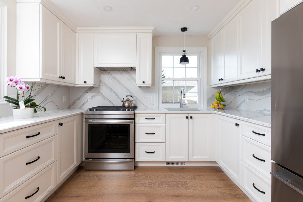 Inspiration for a transitional u-shaped medium tone wood floor and brown floor kitchen remodel with white cabinets, quartz countertops, white backsplash, quartz backsplash, white countertops, an undermount sink, recessed-panel cabinets, stainless steel appliances and no island