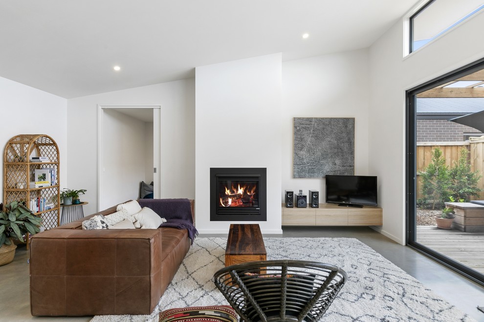 Inspiration for a mid-sized contemporary open concept living room in Geelong with white walls, concrete floors, a standard fireplace, a plaster fireplace surround, a freestanding tv and grey floor.